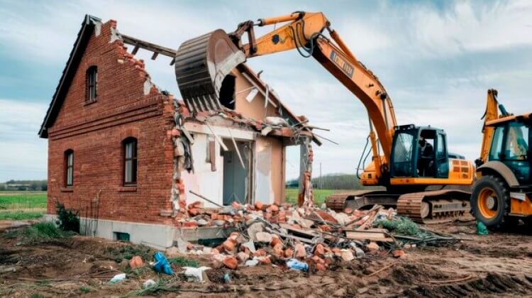 Excavatrice détruisant une maison en briques sur le terrain à la campagne
